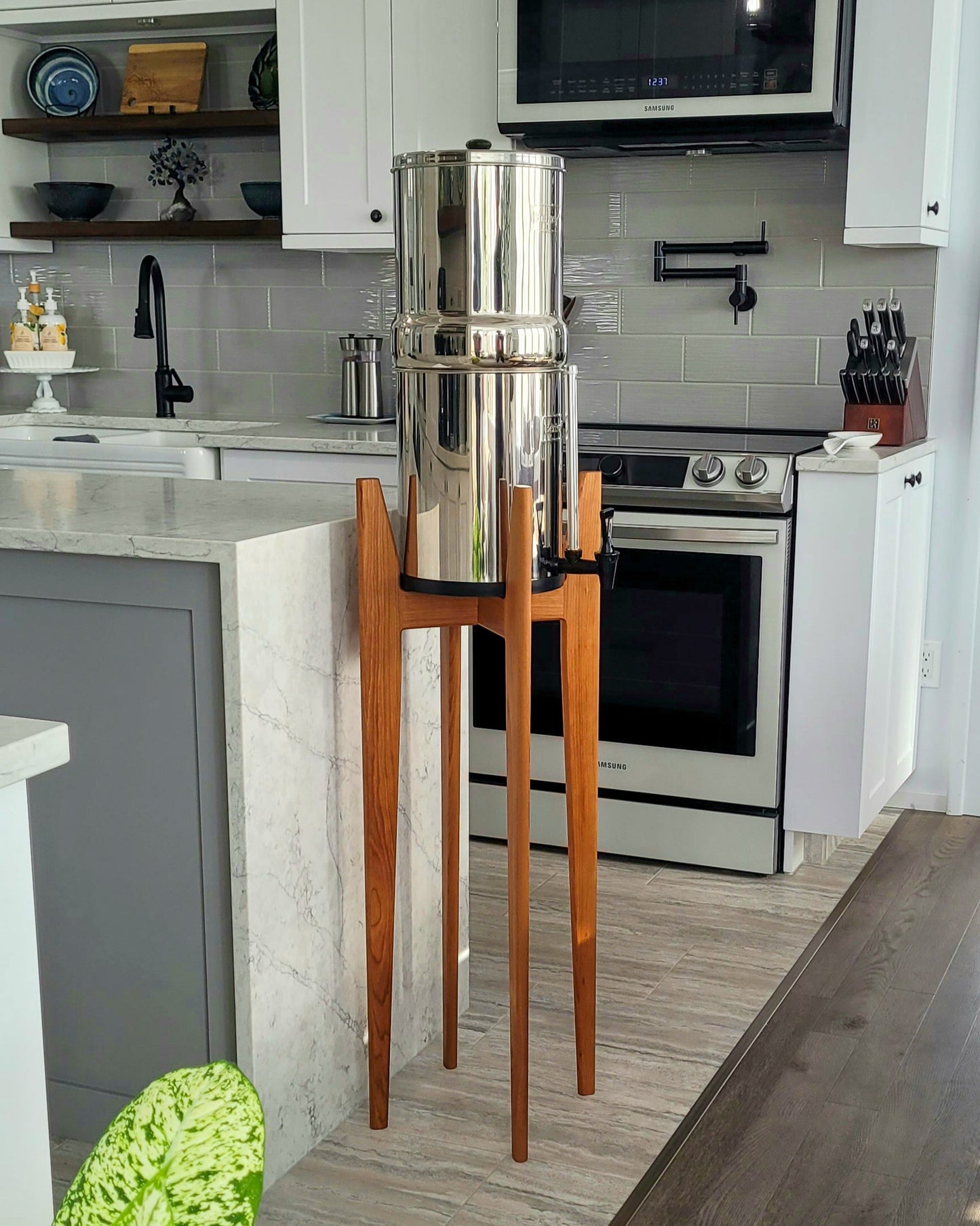 a tall hardwood stand with a stainless steel water filter on it in a light coloured kitchen setting