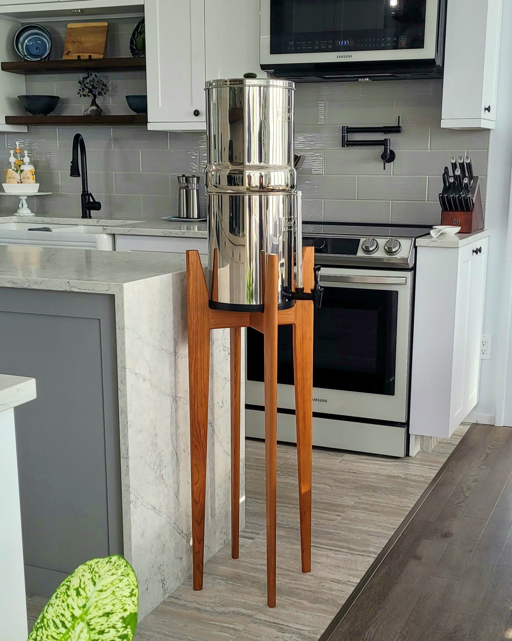 a tall hardwood stand with a stainless steel water filter on it in a light coloured kitchen setting