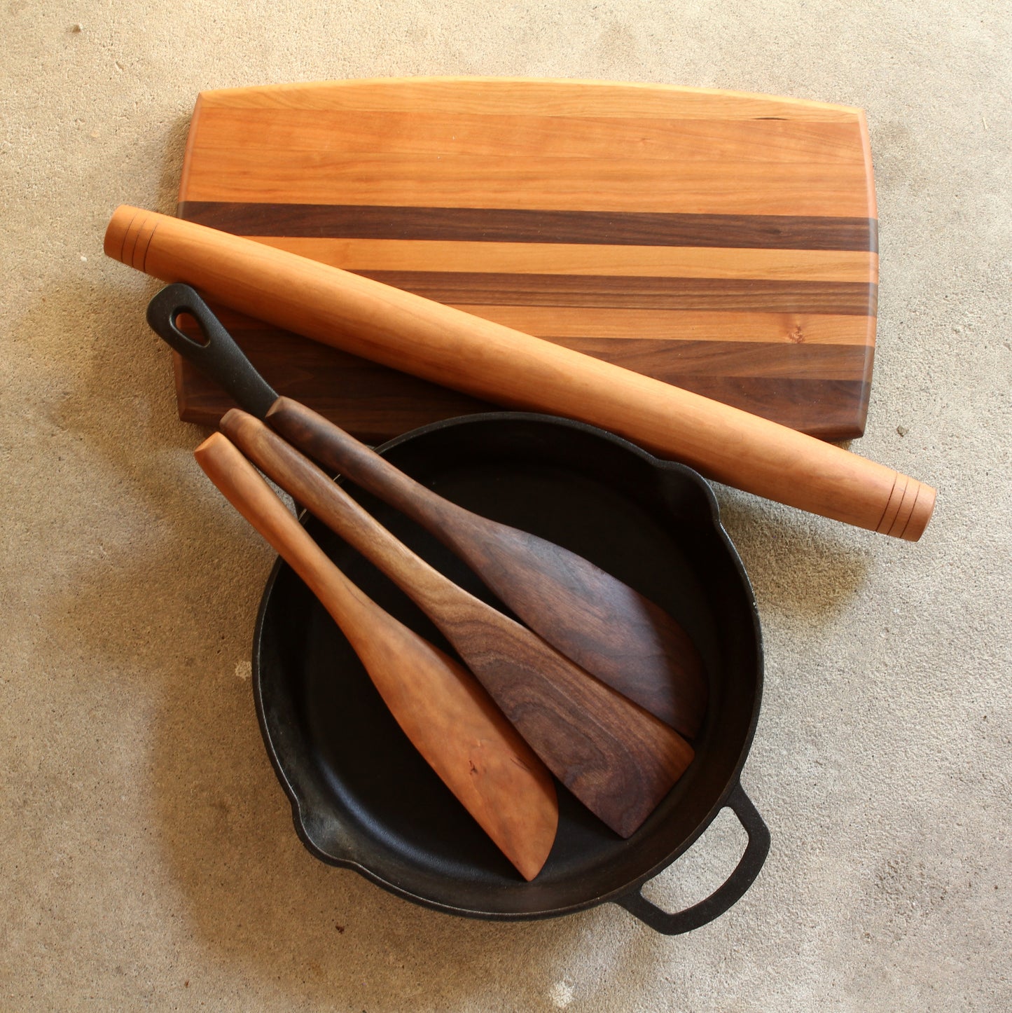 A five piece set including a cutting board made with cherry and walnut wood a cherry rolling pin and 3 cherry spatulas each with a different width and end shape
