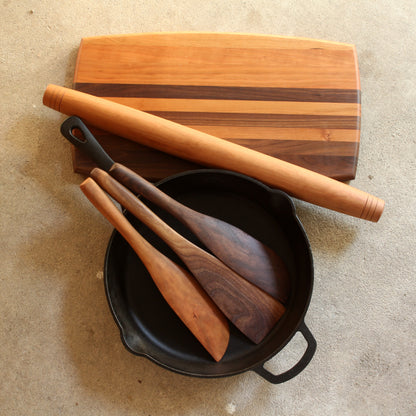 A five piece set including a cutting board made with cherry and walnut wood a cherry rolling pin and 3 cherry spatulas each with a different width and end shape