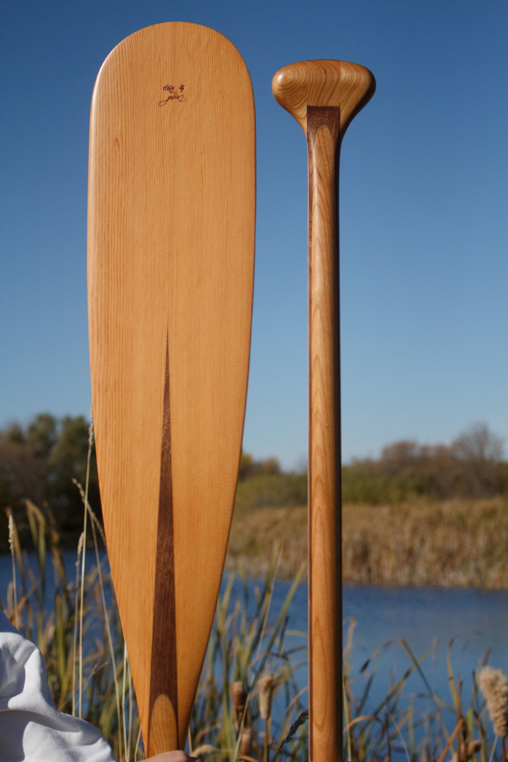 a beavertail canoe paddle that has a light colored blade and a dark inlay for the grip and shaft. made with BC fir and walnut and cherry hardwood. the picture shows a detail of the grip and blade